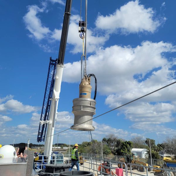 Submersible pump set being lowered by crane into a wet well