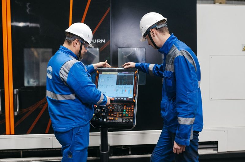 Two technicians in coveralls at a robot teach pendant on a plant floor