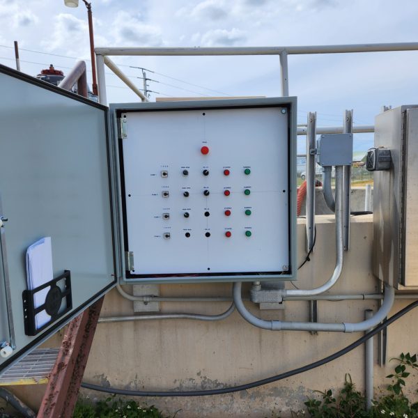 Field-installed control panel with pilot lights and selector switches, door open at a pump station
