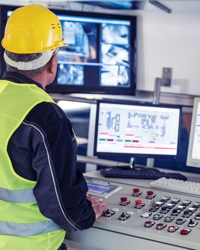 Operator in a high-visibility vest at a control room console with SCADA screens
