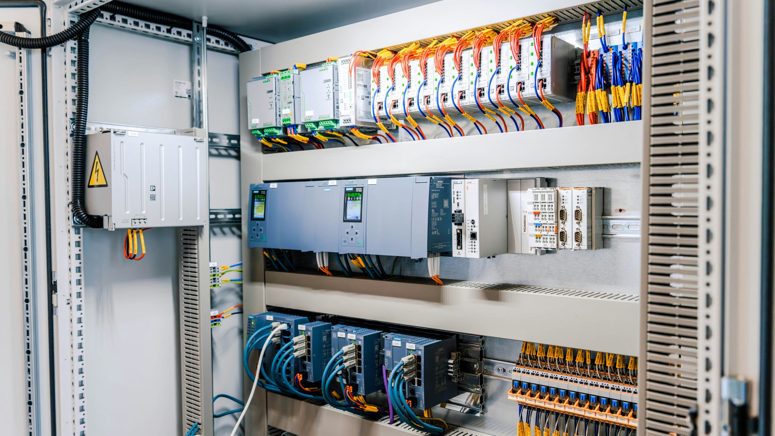 Interior of an assembled control panel with PLCs on DIN rail, circuit breakers, terminal blocks and wiring duct